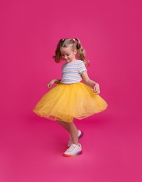 Cute little girl in tutu skirt dancing on pink background