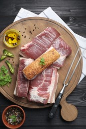 Pieces of raw pork belly, chili pepper, peppercorns, oil and parsley on black wooden table, top view