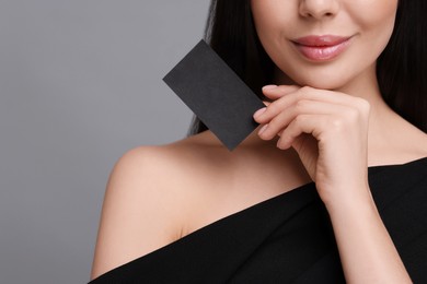 Woman holding blank business card on grey background, closeup. Space for text