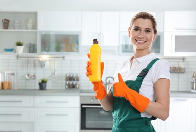 Photo of Portrait of young woman with bottle of detergent in kitchen. Cleaning service