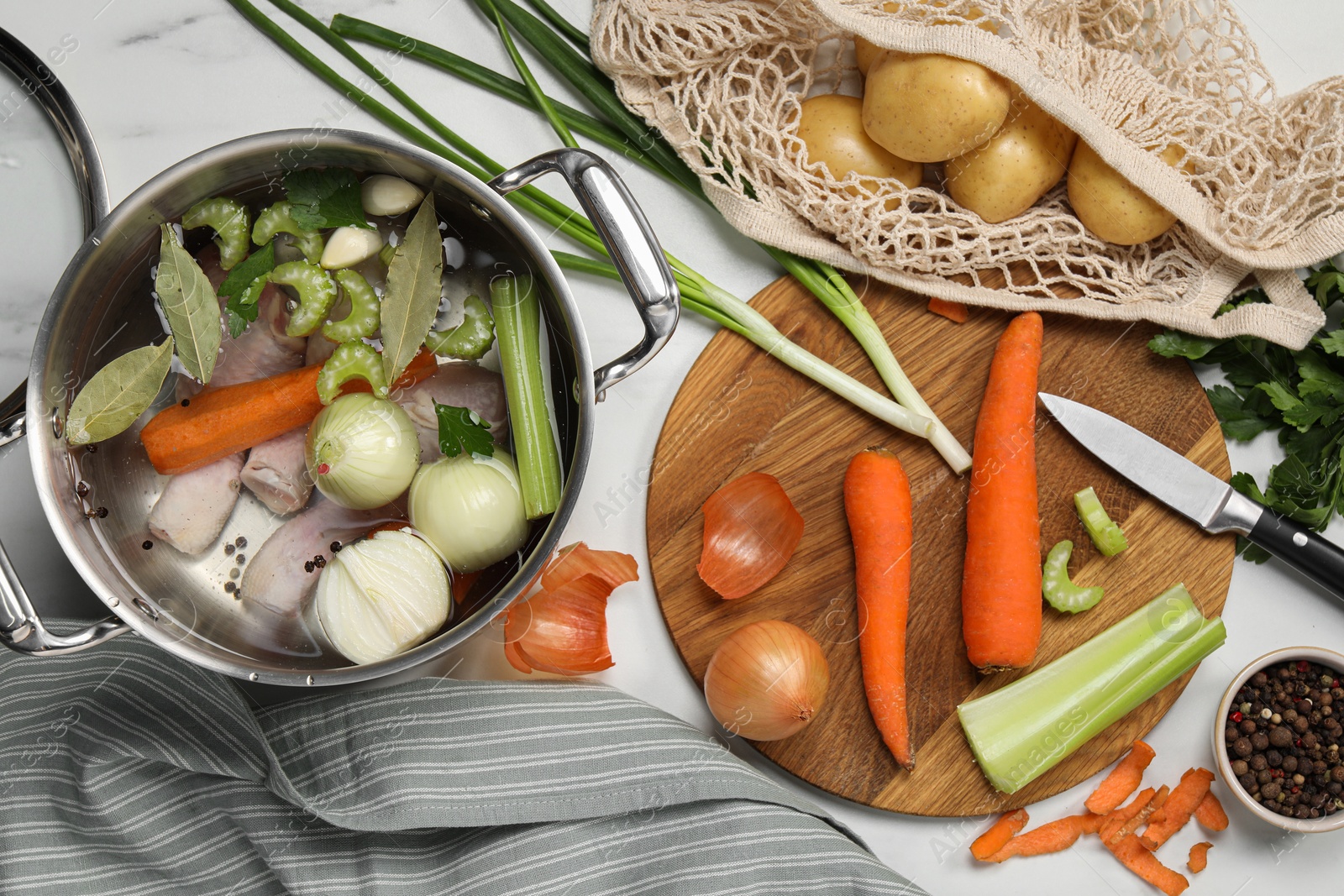 Photo of Pot and different ingredients for cooking tasty bouillon on white marble table, flat lay