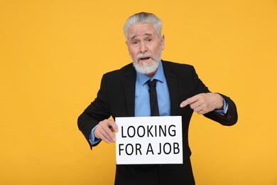 Photo of Unemployed senior man pointing at cardboard sign with phrase Looking For A Job on yellow background