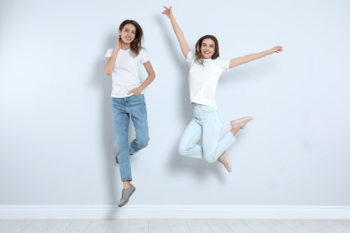 Photo of Young women in stylish jeans jumping near light wall
