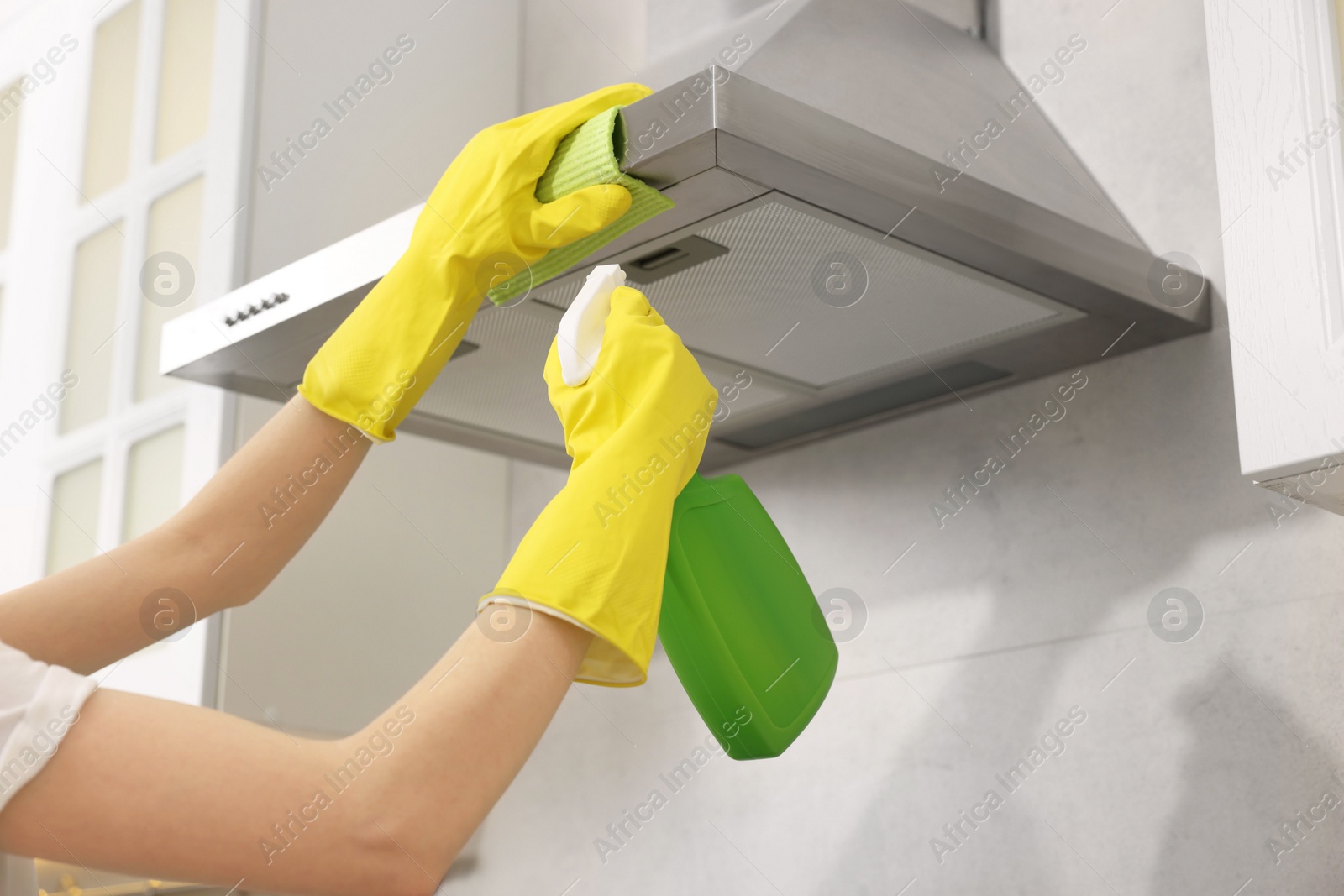 Photo of Woman with spray bottle and microfiber cloth cleaning kitchen hood indoors, closeup