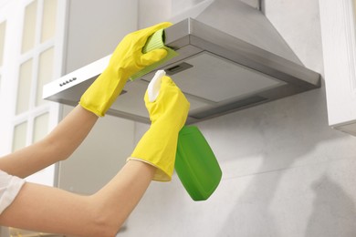 Woman with spray bottle and microfiber cloth cleaning kitchen hood indoors, closeup