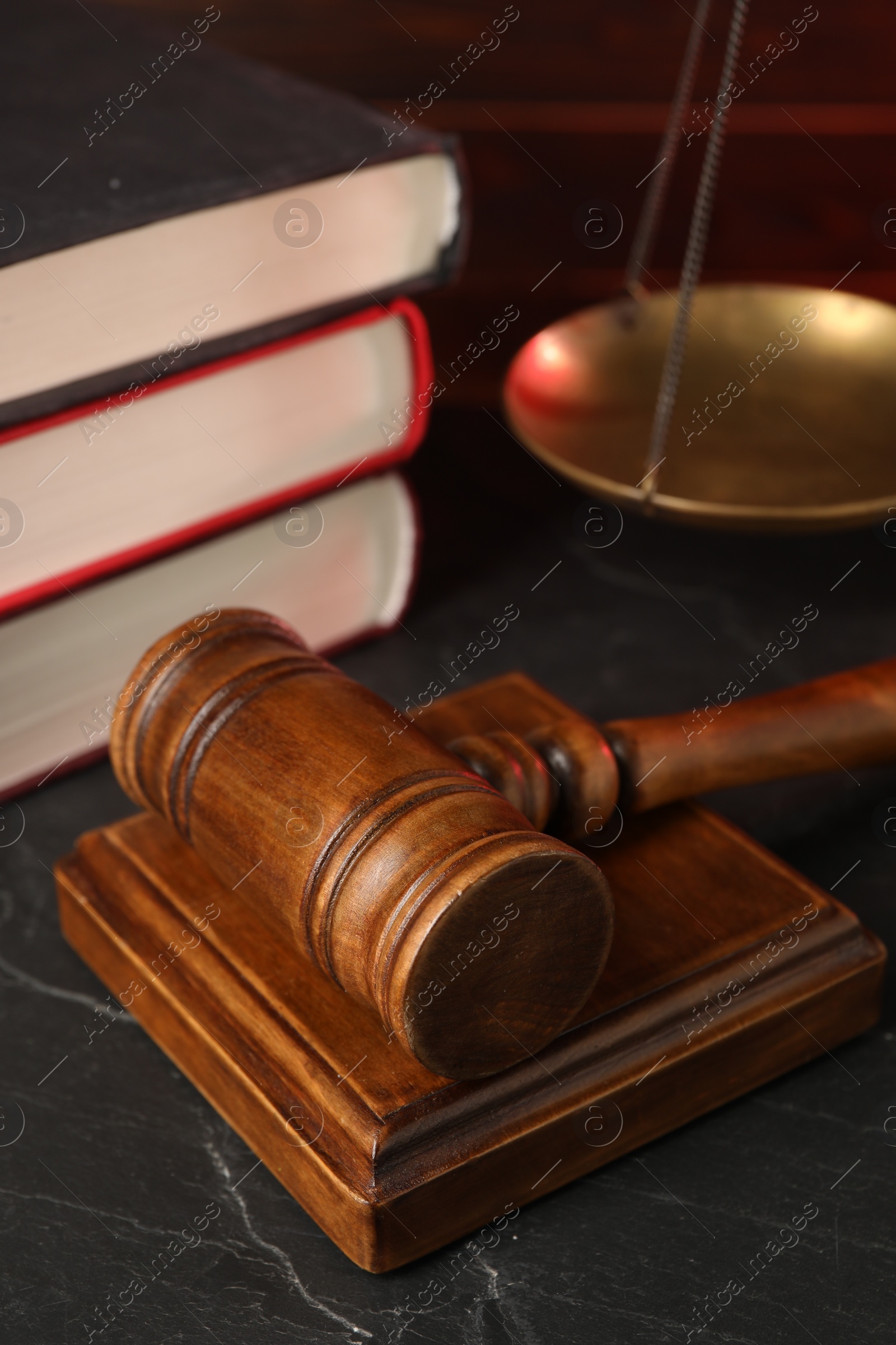 Photo of Wooden gavel and stack of books on dark textured table, closeup