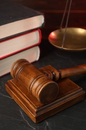 Wooden gavel and stack of books on dark textured table, closeup