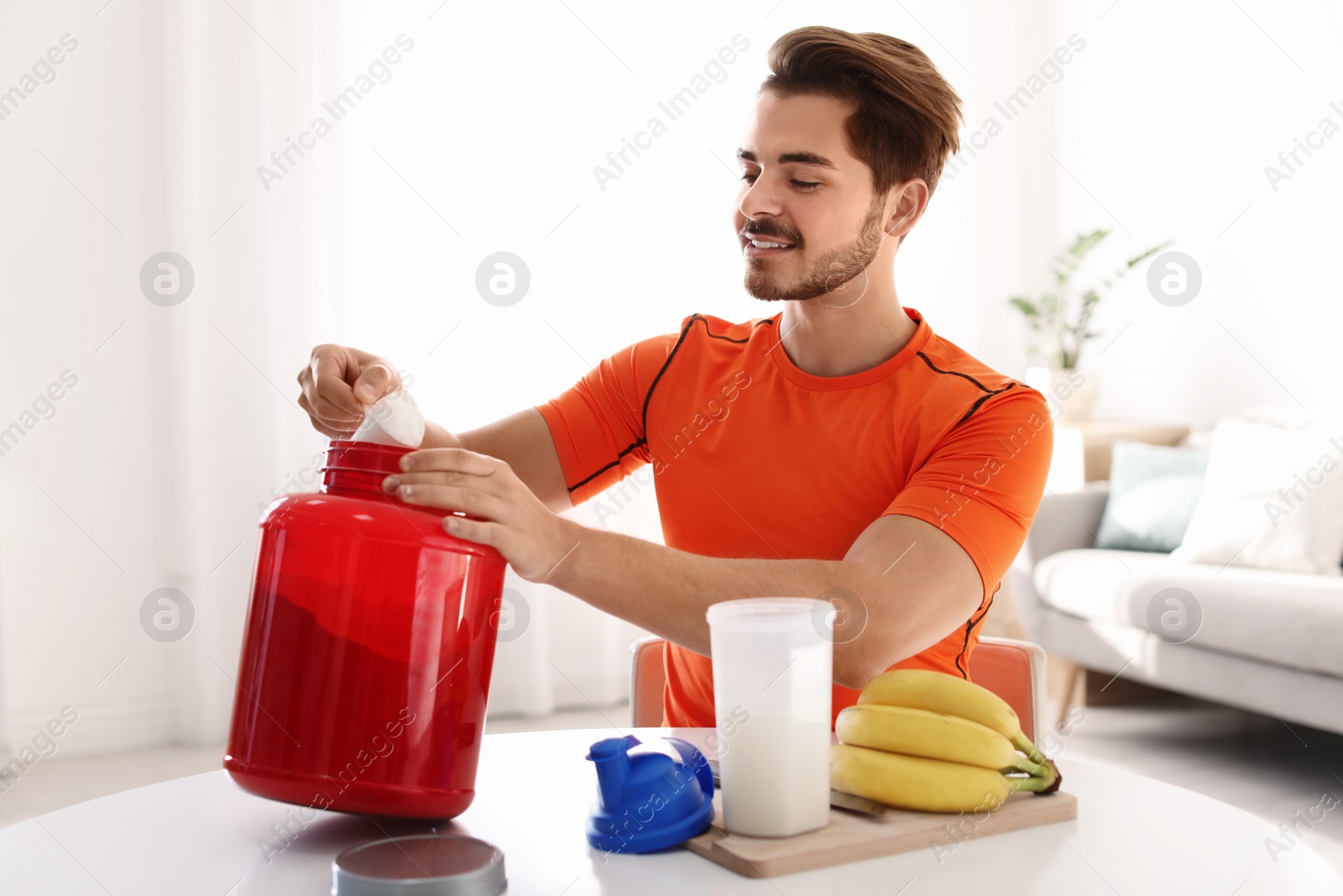 Photo of Young man preparing protein shake at table in room