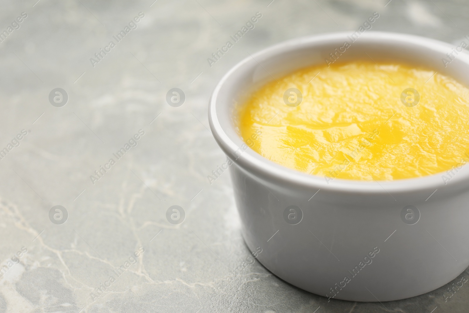 Photo of Ceramic bowl with clarified butter on grey background. Space for text