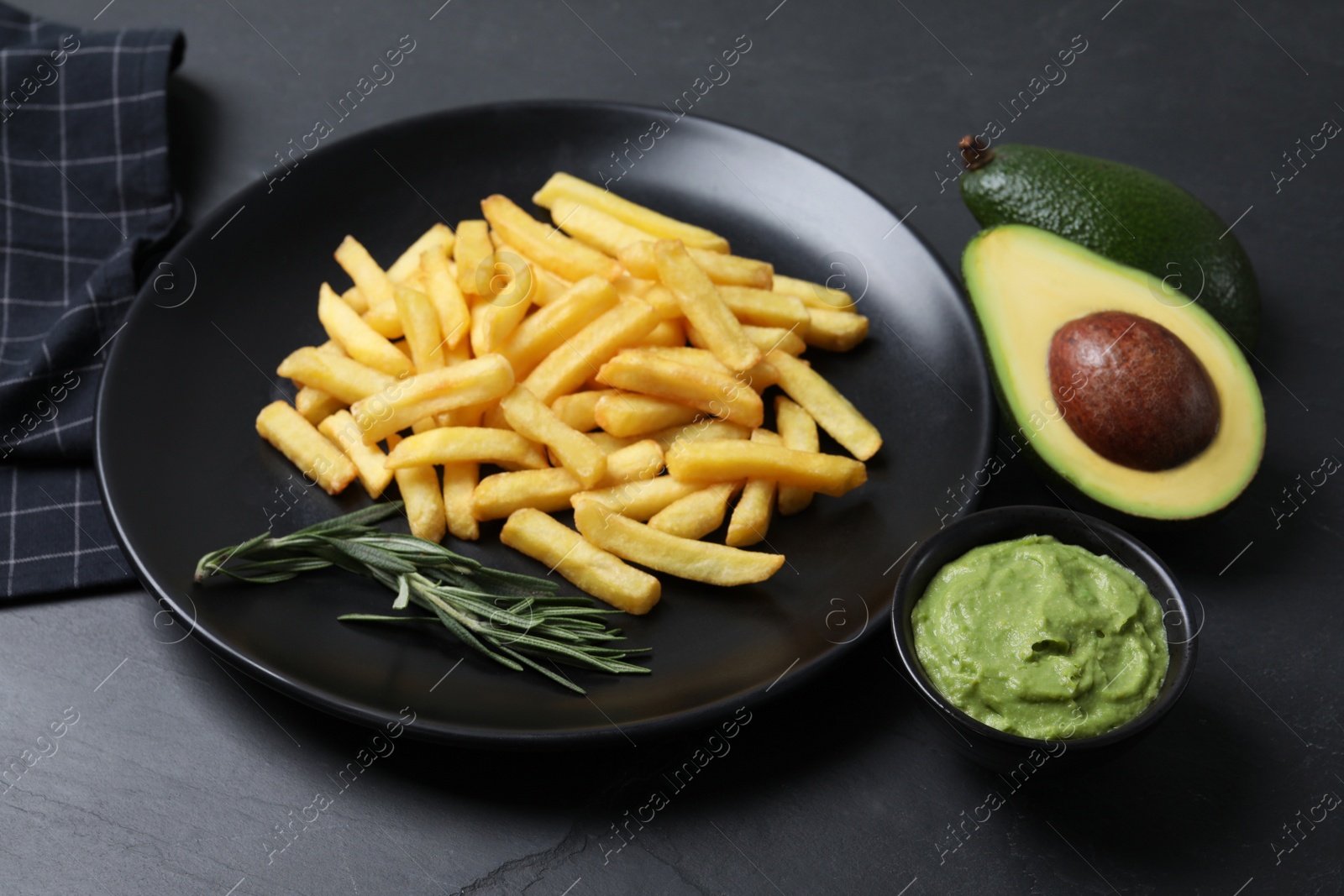 Photo of Plate with french fries, guacamole dip, rosemary and avocado served on black table