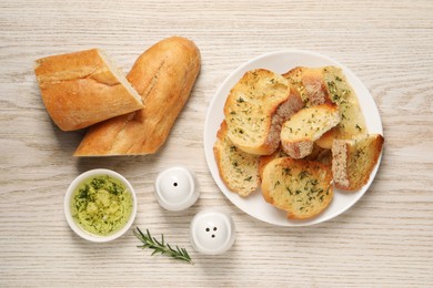 Tasty baguette with garlic and dill served on white wooden table, flat lay