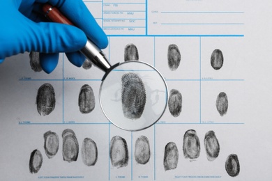 Criminalist studying fingerprints with magnifying glass, top view