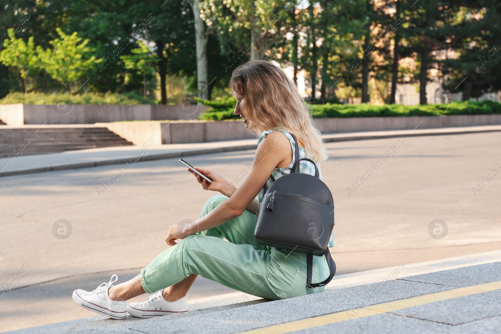 Photo of Young woman with stylish backpack and smartphone on stairs outdoors