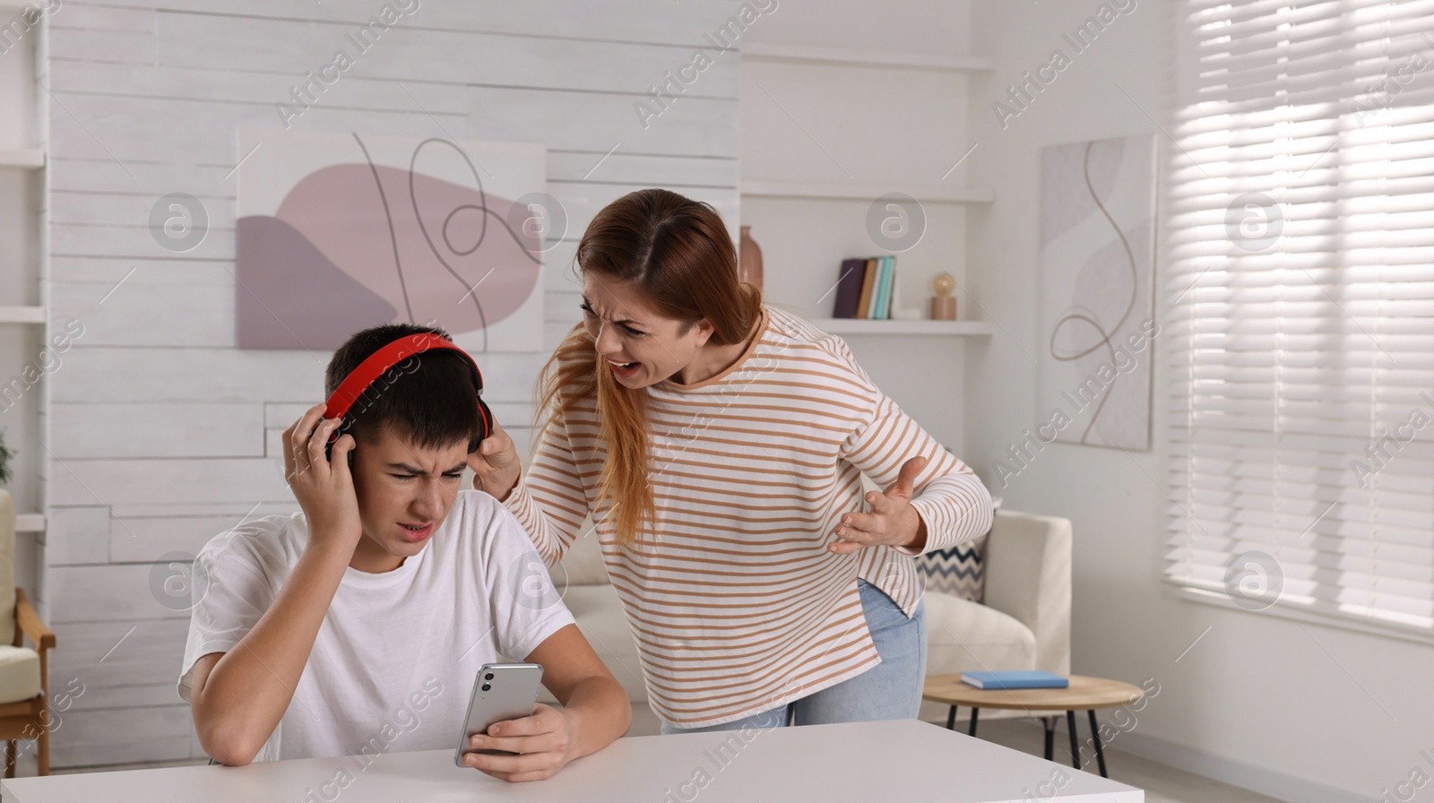 Photo of Mother scolding her son while he listening music in headphones at home. Teenager problems