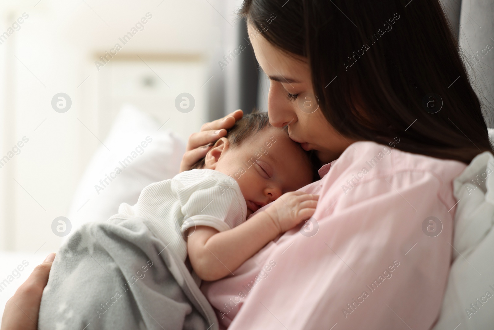 Photo of Mother kissing her sleeping newborn baby in bed at home