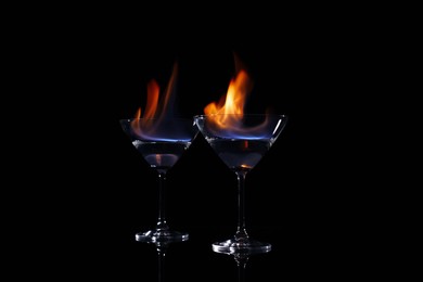 Photo of Cocktail glasses with flaming vodka on black background