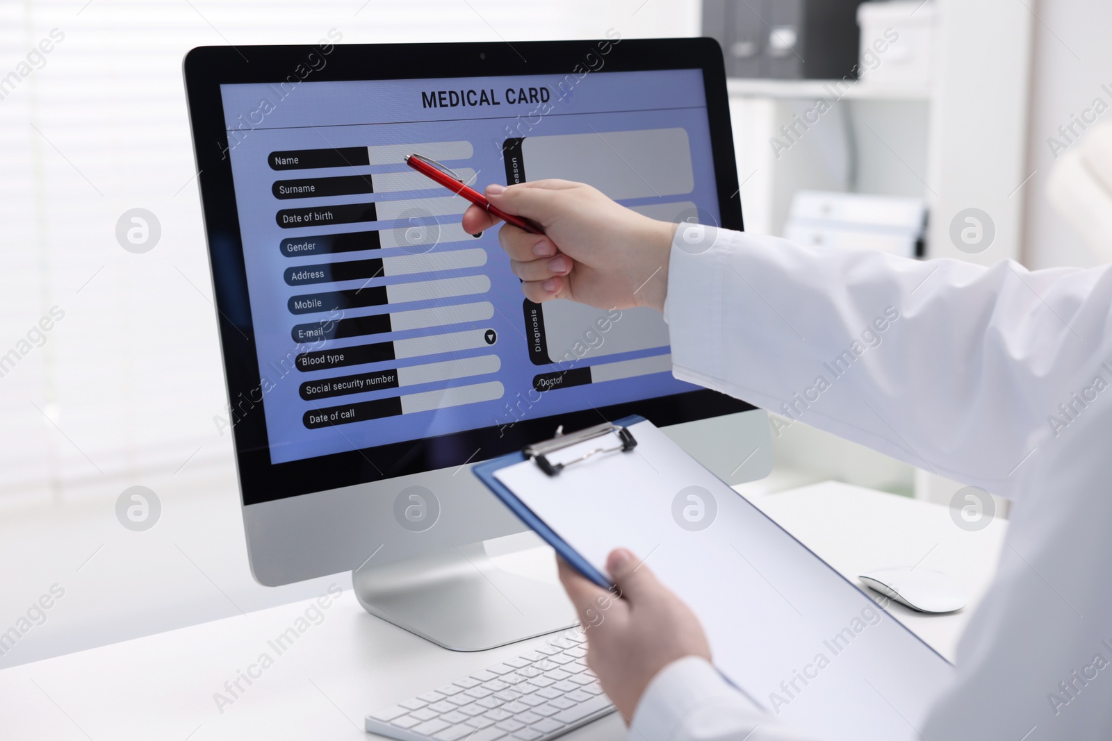 Photo of Doctor using computer to fill out patient's medical card at table in clinic, closeup