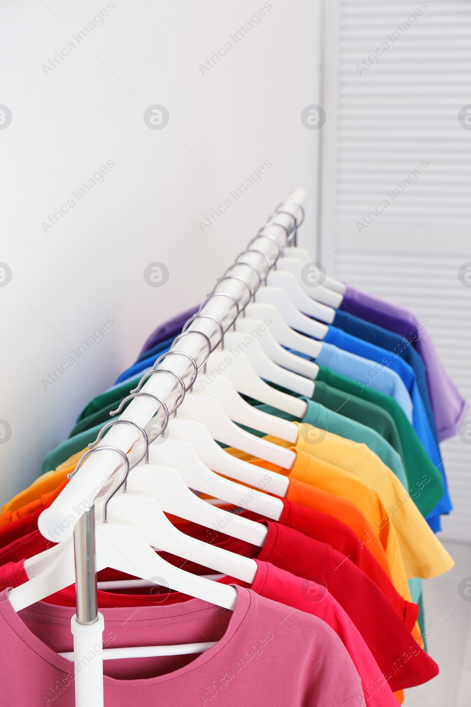 Photo of Rack with bright clothes in room. Rainbow colors