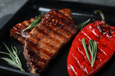 Tasty barbecued meat steak with garnish on grill pan, closeup