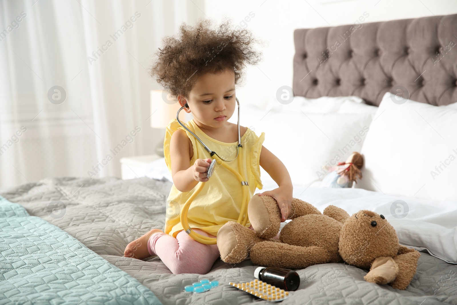 Photo of Cute African American child imagining herself as doctor while playing with stethoscope and toy bunny at home