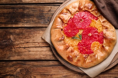 Photo of Tasty galette with citrus fruits and rosemary on wooden table, top view. Space for text