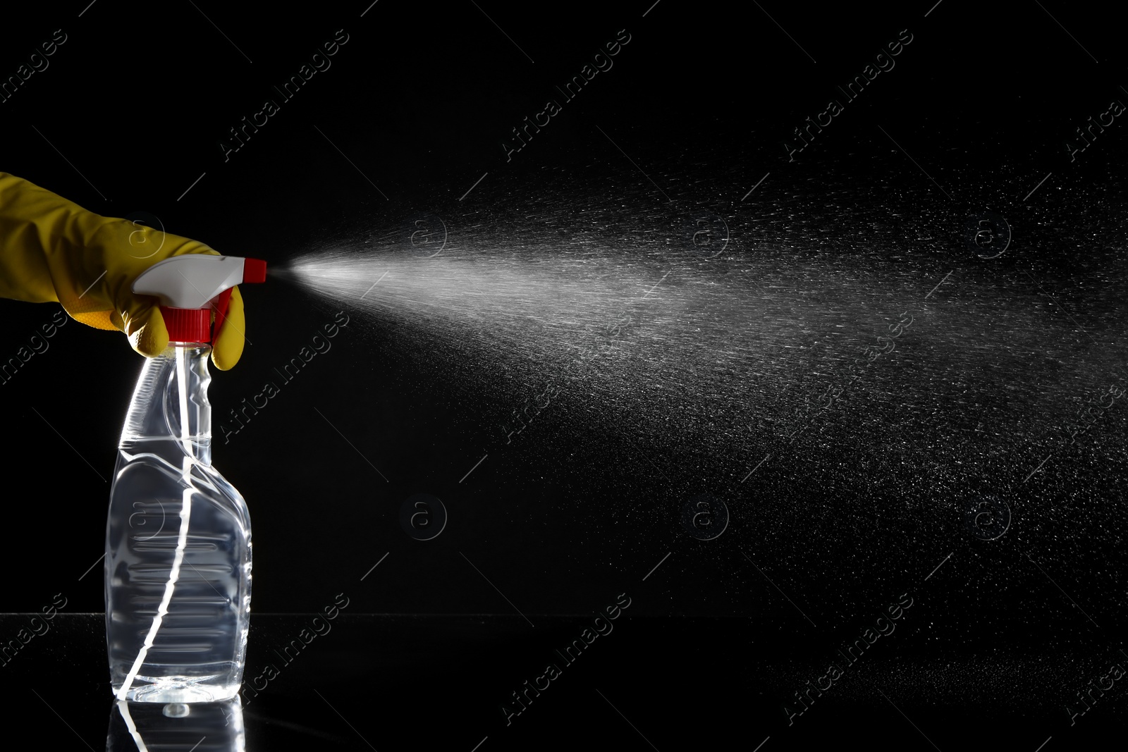 Photo of Woman spraying liquid from bottle on black background, closeup