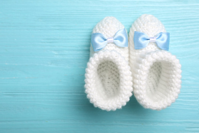 Knitted child's booties on light blue wooden background, top view