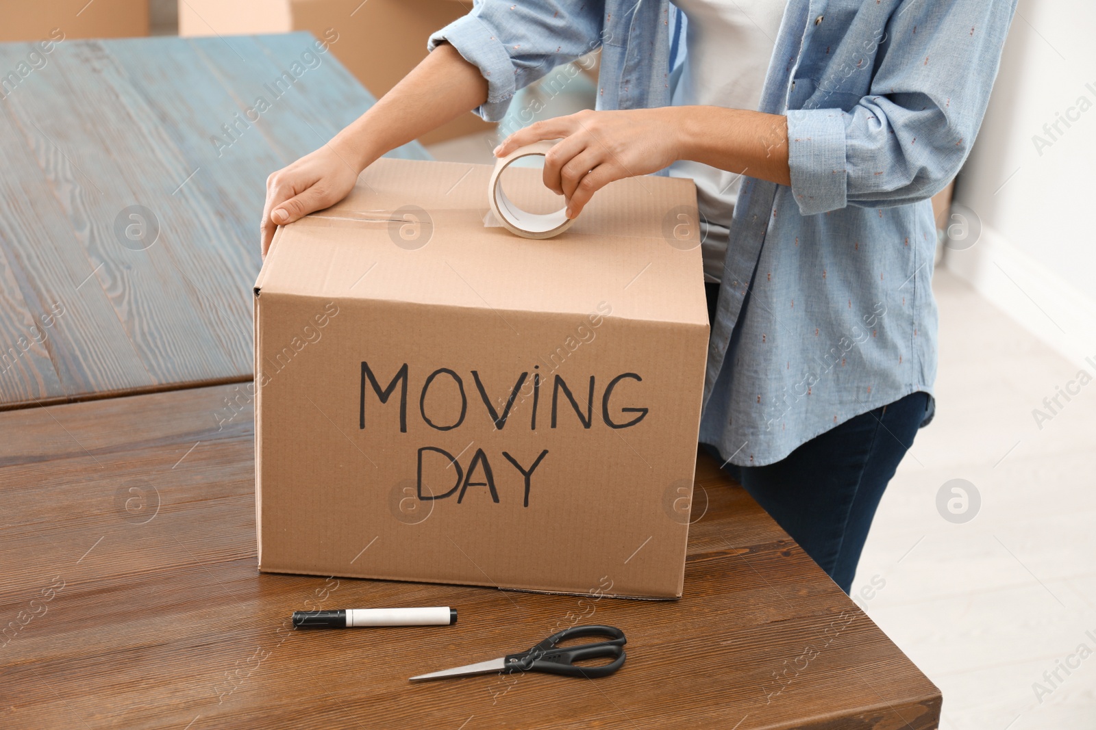 Photo of Woman packing box with words MOVING DAY at wooden table, closeup