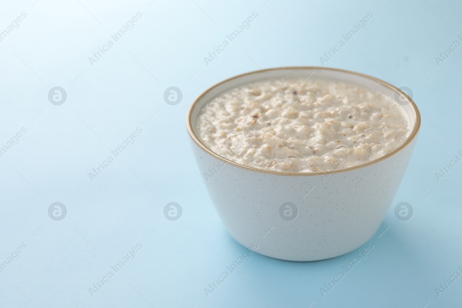 Photo of Tasty boiled oatmeal in bowl on light blue table, space for text