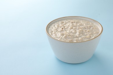 Photo of Tasty boiled oatmeal in bowl on light blue table, space for text