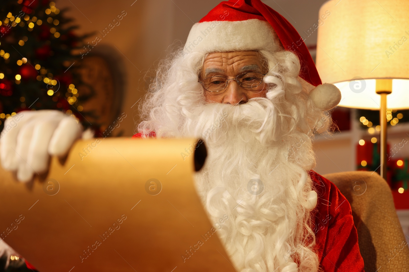 Photo of Santa Claus reading letter in room decorated for Christmas
