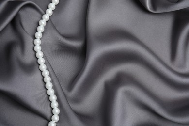 Photo of Beautiful pearls on grey silk, top view. Space for text