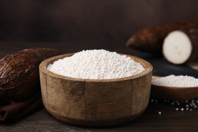 Photo of Tapioca pearls in bowl and cassava roots on wooden table, closeup