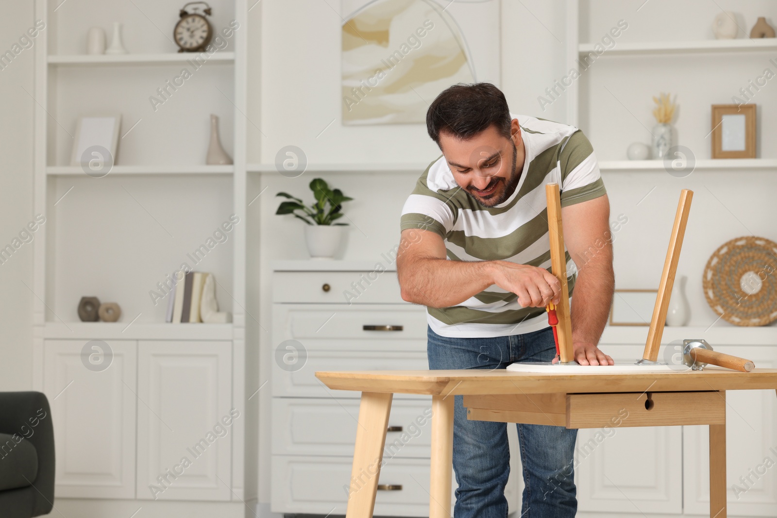 Photo of Man with screwdriver assembling furniture at table in room. Space for text