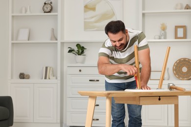 Man with screwdriver assembling furniture at table in room. Space for text