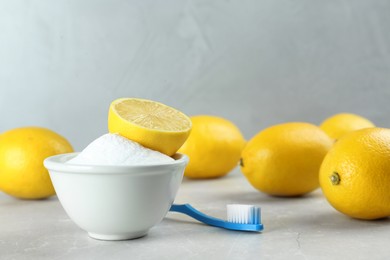 Toothbrush, lemons and bowl of baking soda on light grey table