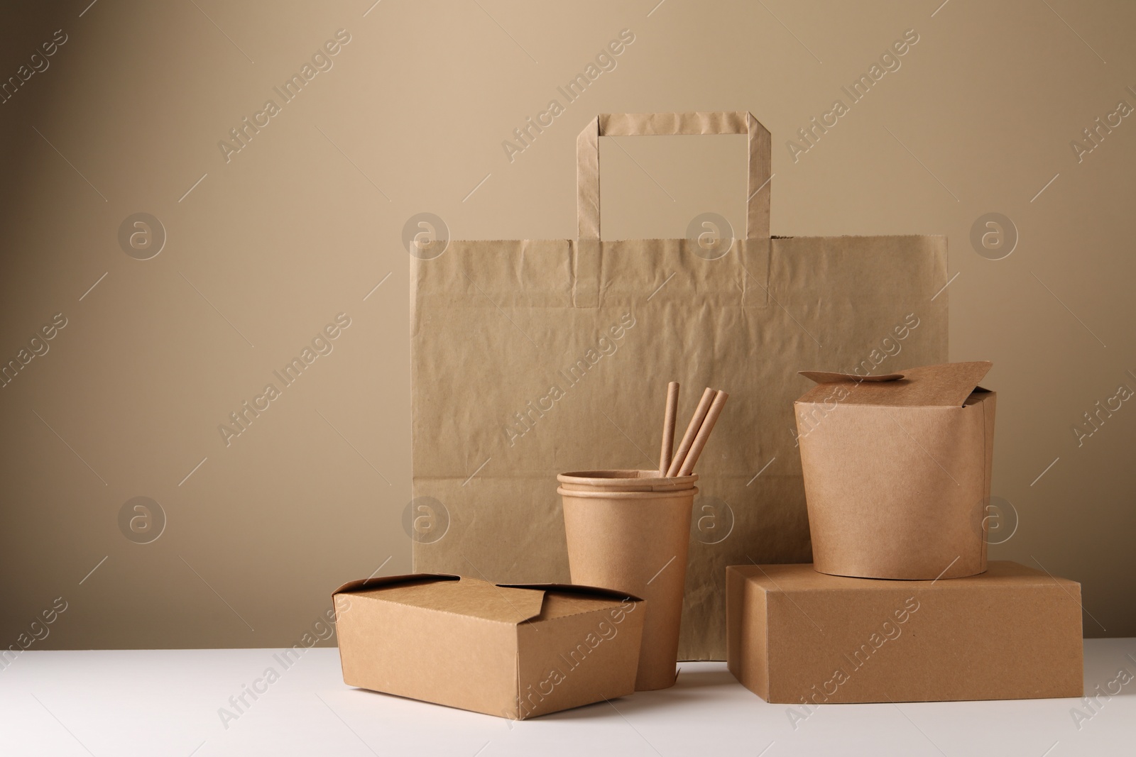 Photo of Eco friendly food packaging. Paper containers, bag and straws on white table against beige background. Space for text