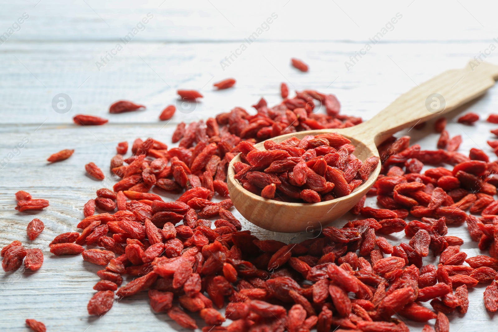 Photo of Spoon and dried goji berries on white wooden table, closeup. Healthy superfood