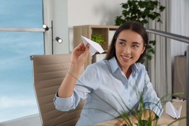 Beautiful young woman playing with paper plane at desk in office