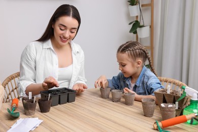 Photo of Mother and her daughter planting vegetable seeds into peat pots with soil at wooden table indoors