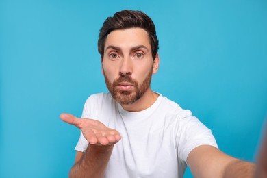 Photo of Handsome man blowing kiss while taking selfie on light blue background