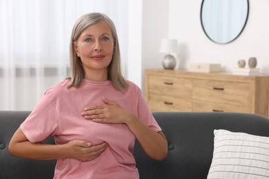 Photo of Beautiful senior woman doing breast self-examination at home, space for text