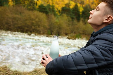 Boy holding thermo bottle with drink in beautiful mountains