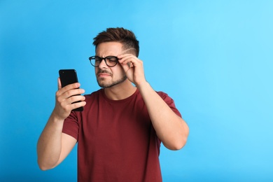Photo of Young man with vision problems using smartphone on blue background, space for text