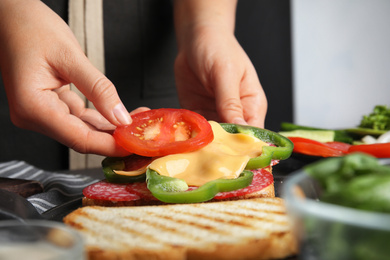 Photo of Woman adding tomato to sandwich at table, closeup