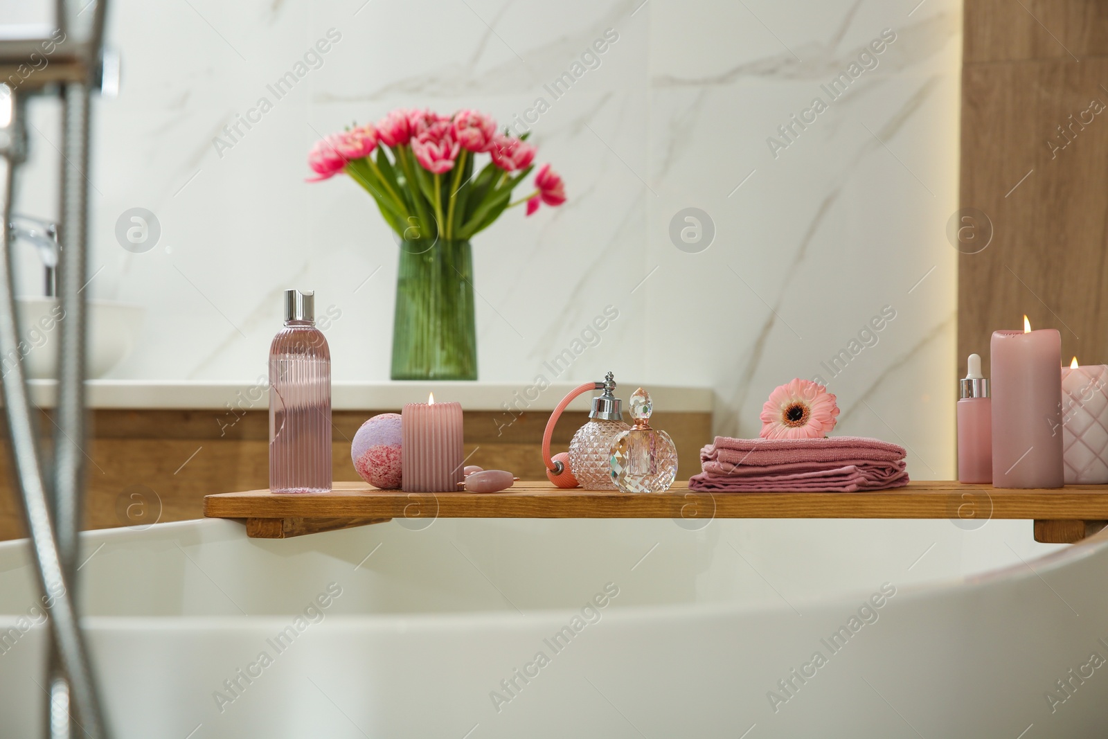 Photo of Wooden bath tray with candles and personal care products on tub indoors