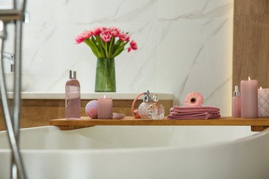 Photo of Wooden bath tray with candles and personal care products on tub indoors