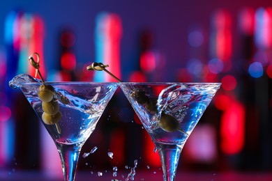 Clinking martini glasses with splashing cocktail and olives in bar, closeup