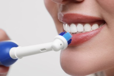 Woman brushing her teeth with electric toothbrush on white background, closeup