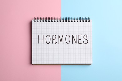 Photo of Notebook with word Hormones on color background, top view